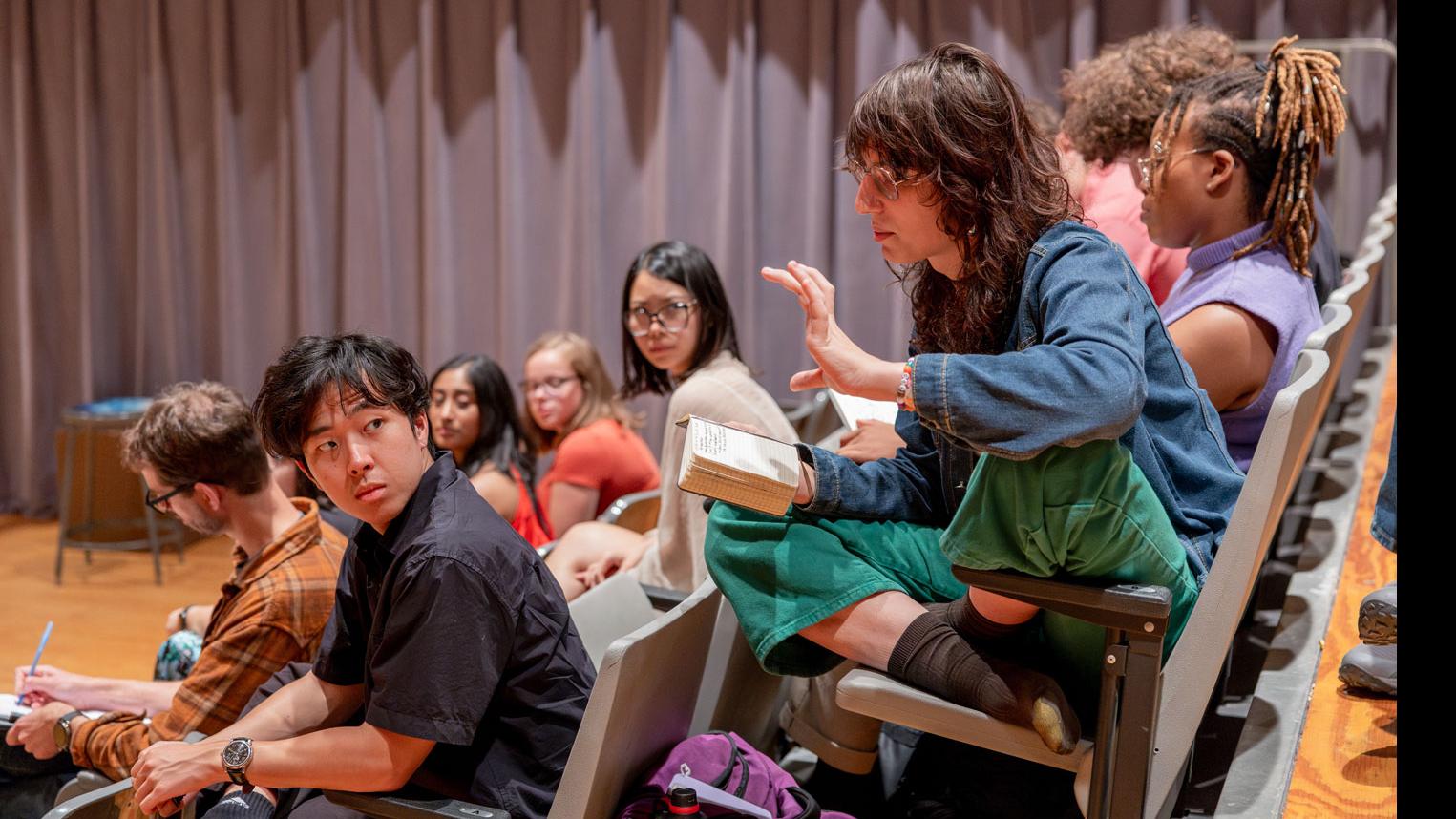 A student sits in the audience and reads from a notebook while other students seated in the audience look on in the Class of ’56 Dance Studio Theatre.