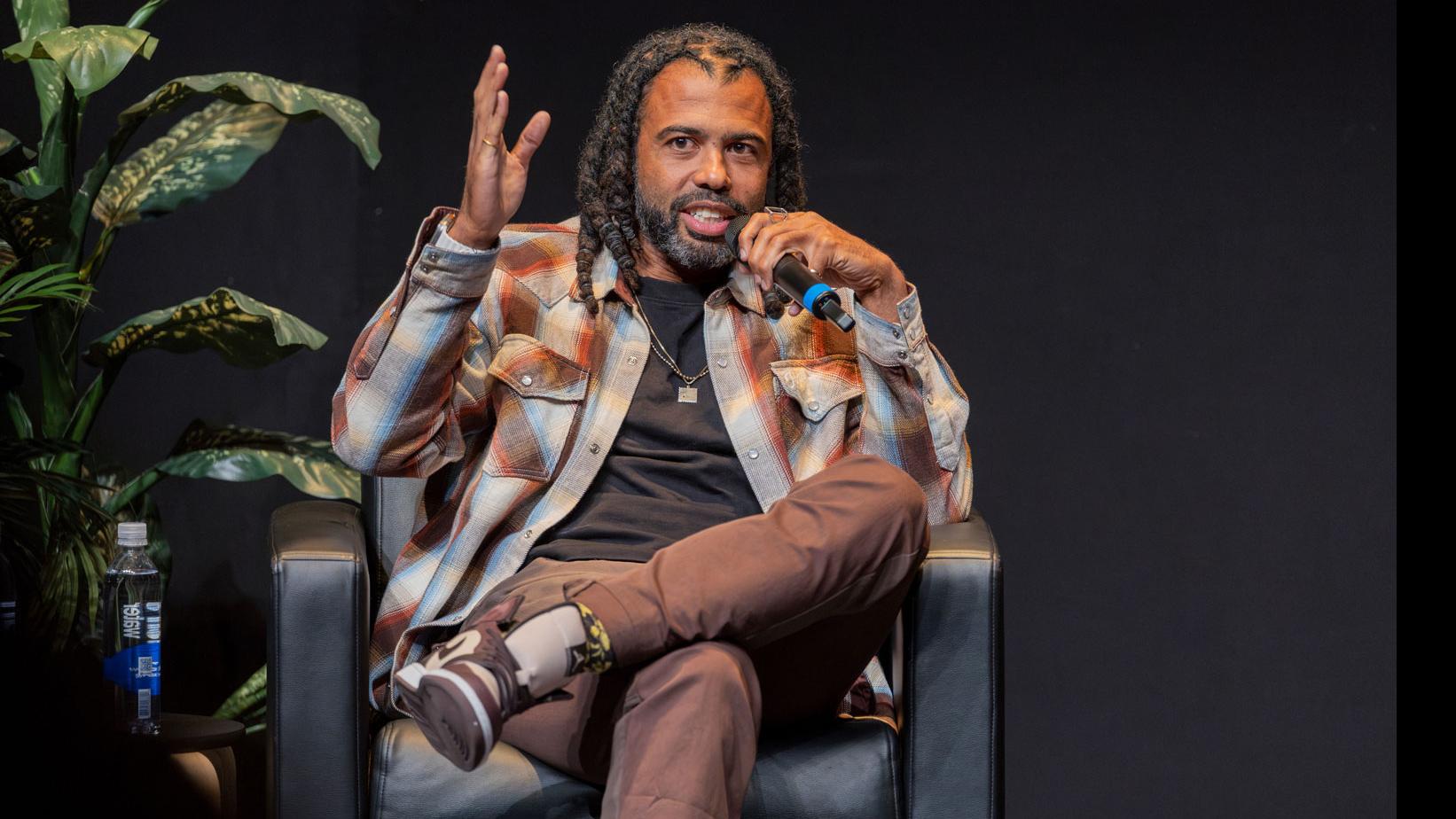 Daveed Diggs sits and speaks into a microphone on stage in the Kiplinger Theatre.