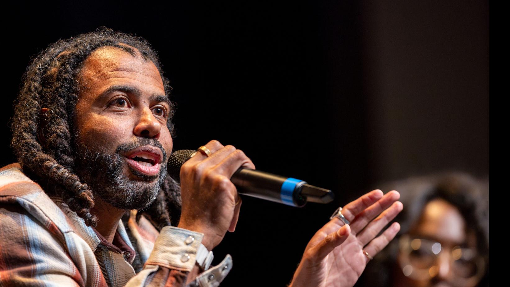 Daveed Diggs sits and speaks into a microphone on stage in the Kiplinger Theatre.