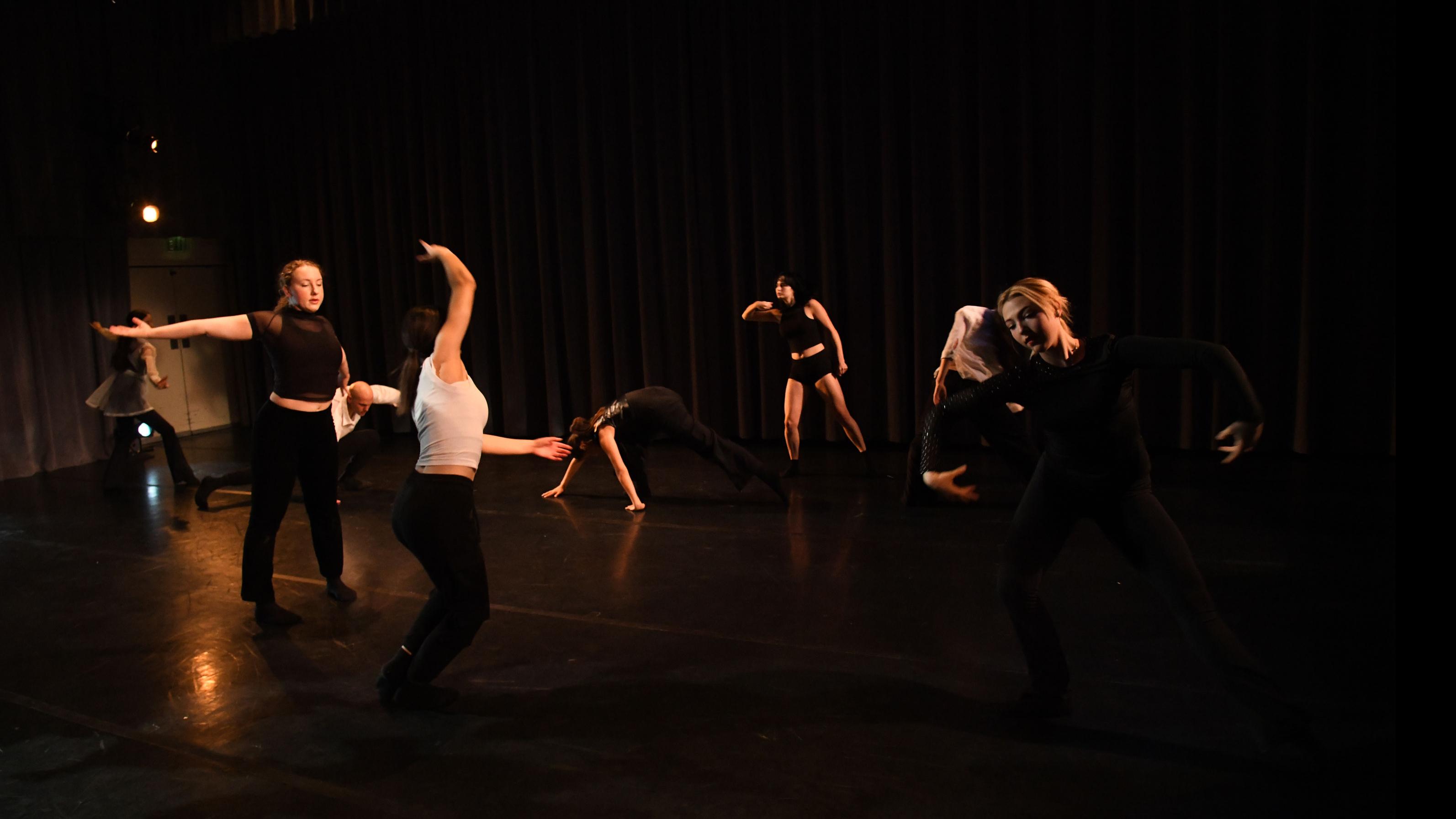 An ensemble of performers spread across the stage in various movement poses, in the Class of ’56 Dance Studio Theatre.