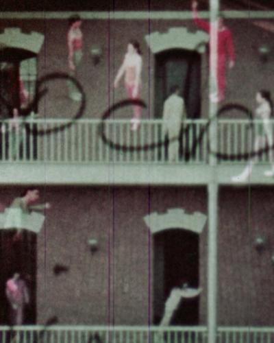 Still from the film “Assemblage” in which there are two floors with railings outside three open doors per floor, with a dozen people in various movement poses floating and blended into the background. 